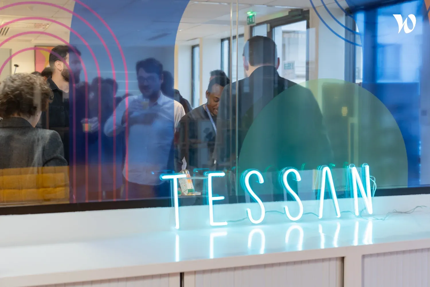The Tessan team gathered behind a glass wall lit by the Tessan neon sign at the Paris office.
