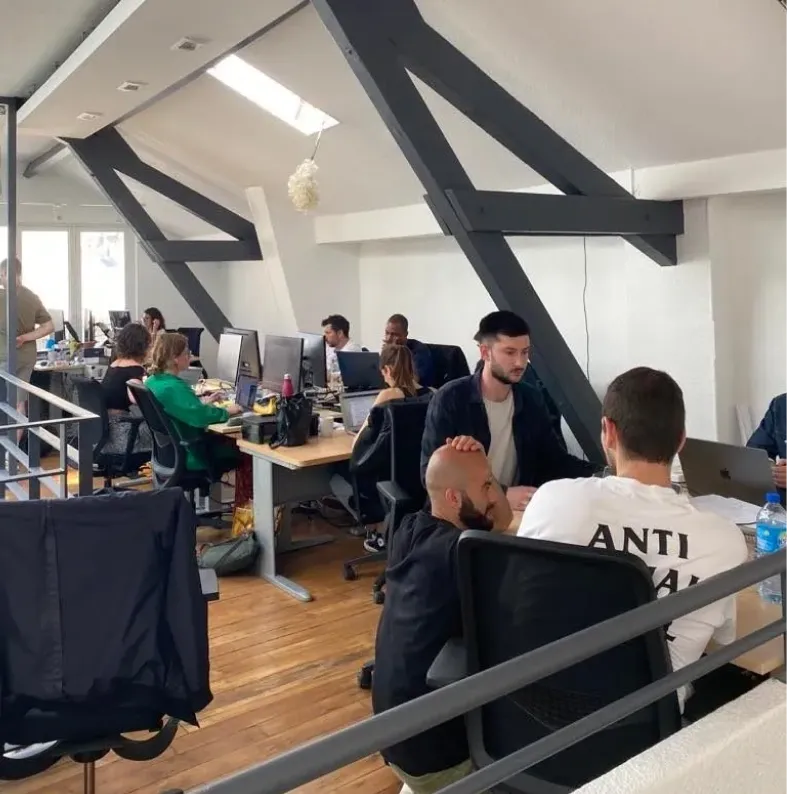 The Tessan open-plan workspace under exposed beams, with the team at their desks.